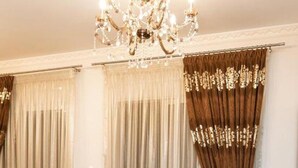 A dining area with a dark wooden table and chairs, a chandelier, and curtains. - Vosinakis House in Volos (Volos)