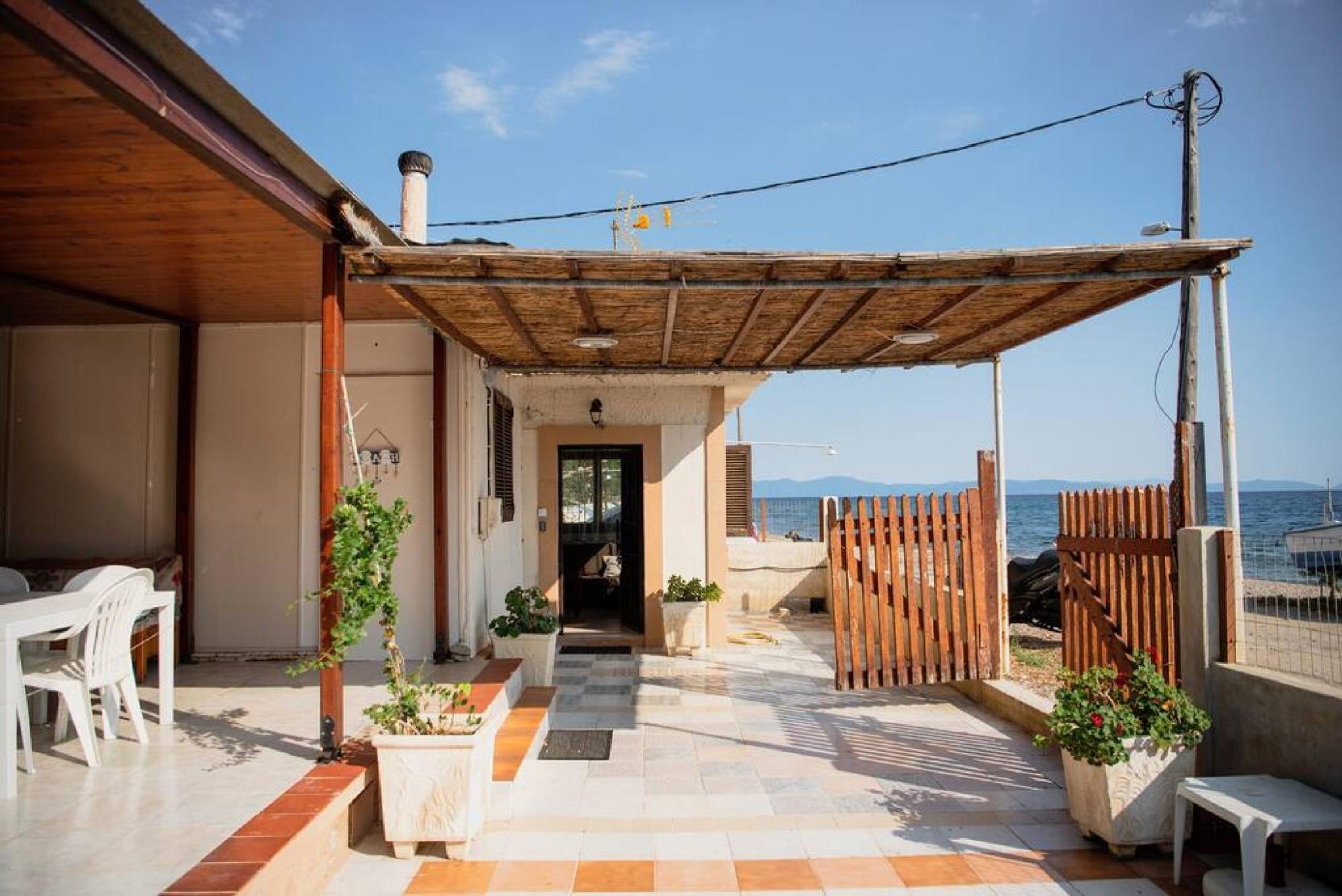 Un espace extérieur abrité, doté d’une pergola en bois, de plantes en pot et offrant une vue sur la mer.