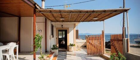 Un espace extérieur abrité, doté d’une pergola en bois, de plantes en pot et offrant une vue sur la mer.
