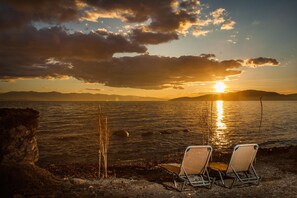 Een zonsondergang uitzicht over een wateroppervlak met twee strandstoelen gericht op het strand.