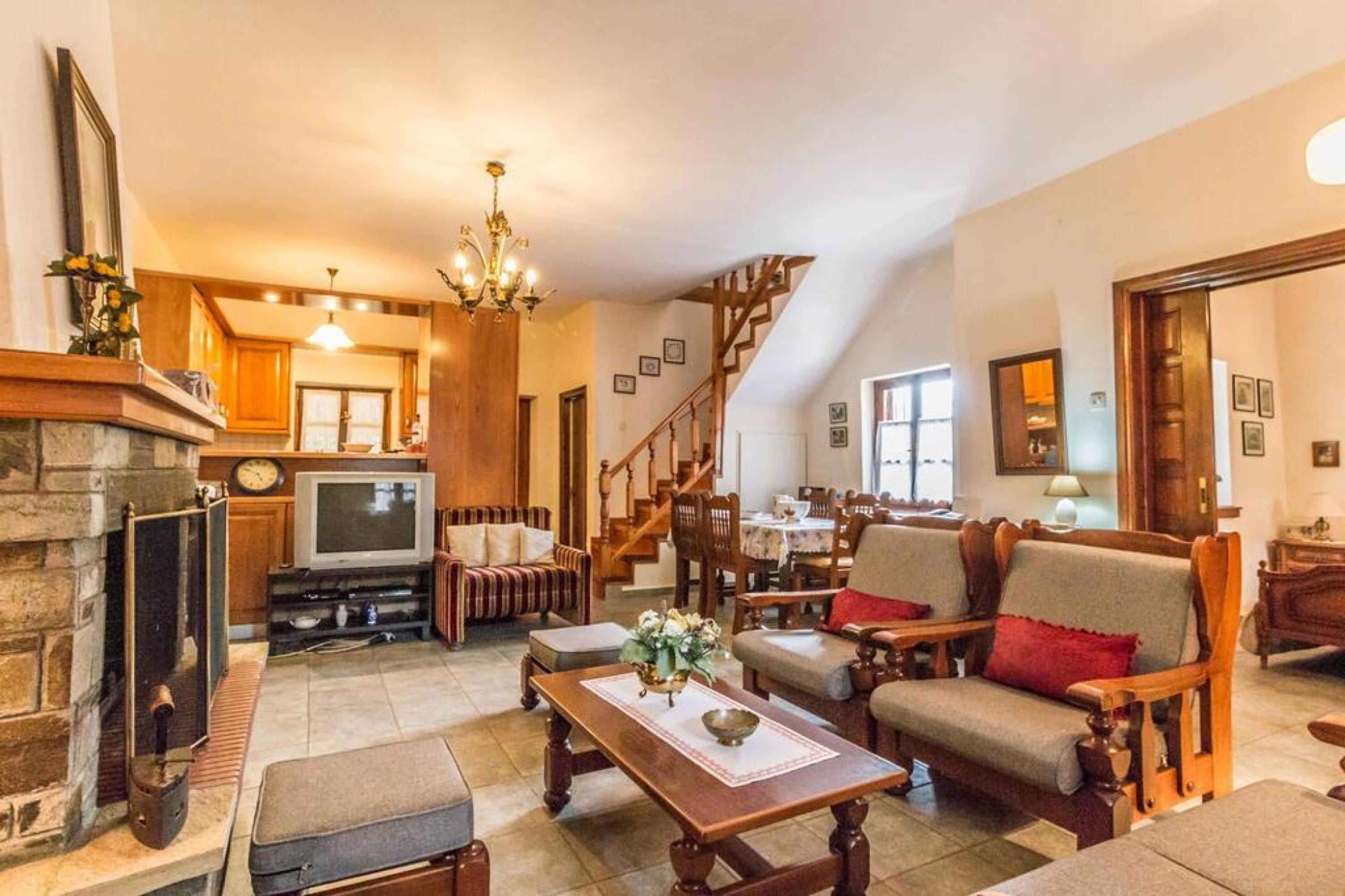 A cozy living room with a fireplace, wooden furniture, a television, and a staircase leading to another level.