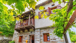A stone building with a balcony, wooden shutters, and potted plants.