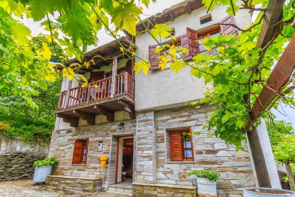 A stone building with a balcony, wooden shutters, and potted plants.