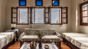 A room with two beds, a sofa, a table with a vase, and three windows with shutters.