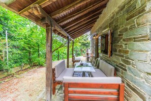 A rustic stone building with a covered patio area featuring wooden furniture and a table.