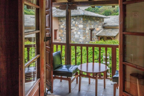 A wooden balcony with a stone wall, a round table, and two chairs.