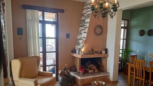 A cozy living room with a fireplace, a comfortable sofa, a dining table with chairs, and a chandelier. - Alonaki Seafront Cottage (Nea Agchialos)