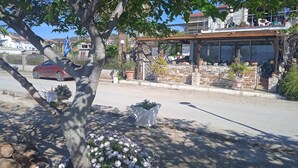 A street view with a building that has a stone facade, a wooden roof, and potted plants. - Alonaki Seafront Cottage (Nea Agchialos)