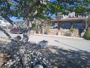 A street view with a building that has a stone facade, a wooden roof, and potted plants. - Alonaki Seafront Cottage (Nea Agchialos)
