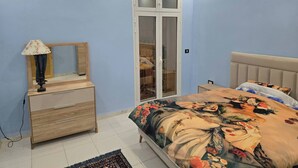 Ein Schlafzimmer mit einem Bett, einem Schminktisch, einem Spiegel und einer Tür mit Glasverzierungen.