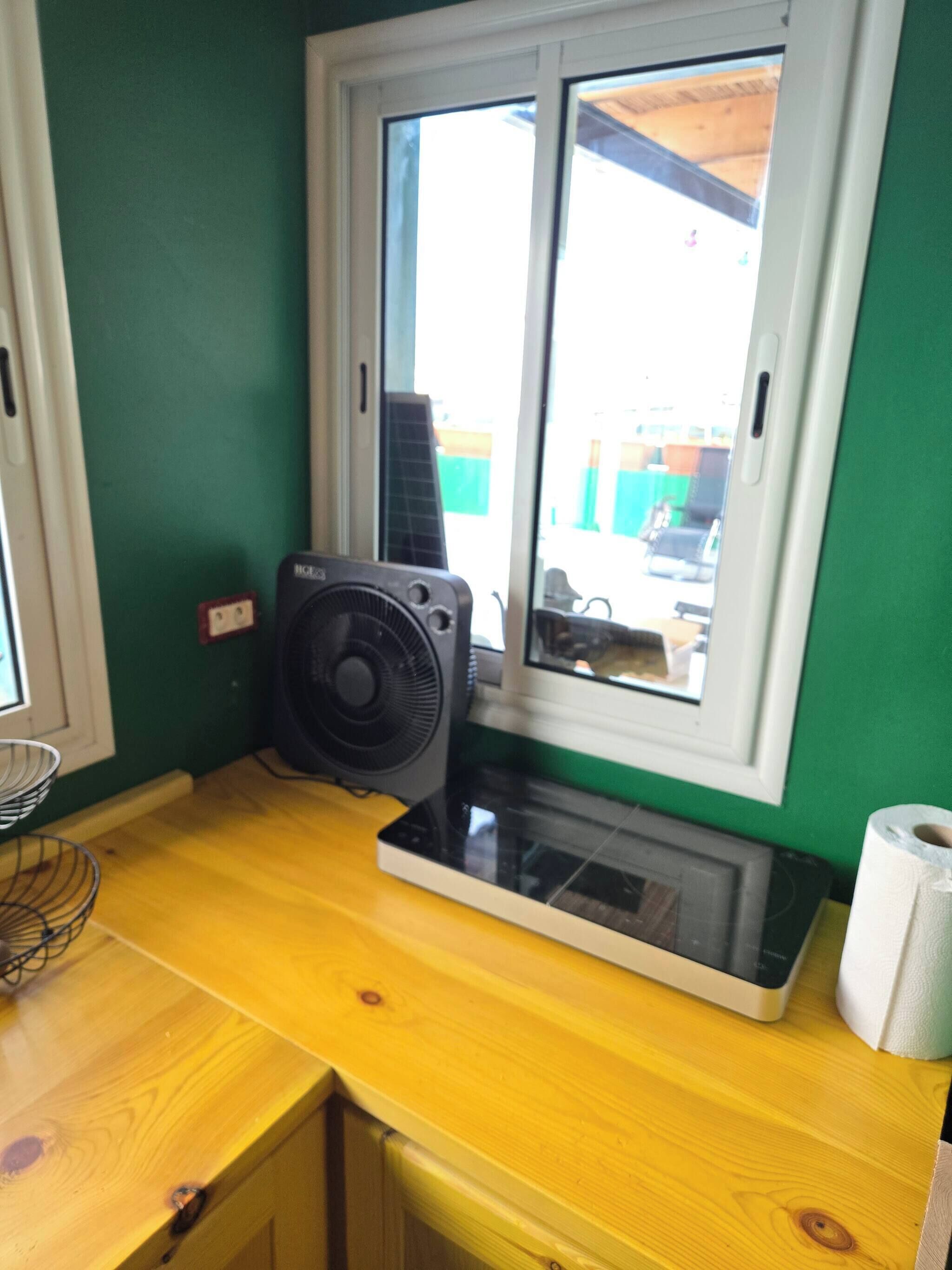 A kitchen with a window, a fan, and a microwave.