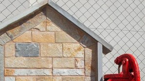 A red fire hydrant next to a stone building with a triangular roof. - Aethra House in Agria Volou (Agria Volou)