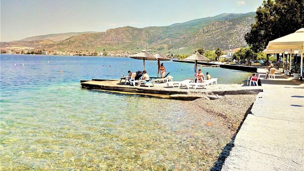 A waterfront area with clear water, a dock with lounge chairs, and a mountainous backdrop. - Aethra House in Agria Volou (Agria Volou)