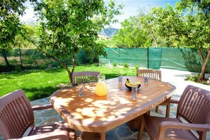 An outdoor wooden table with chairs, a pitcher of orange juice, and a bowl of fruit. - Aethra House in Agria Volou (Agria Volou)