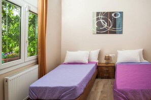 A bedroom with two beds, a window with a view of greenery, a radiator, and a wall-mounted abstract painting. - Aethra House in Agria Volou (Agria Volou)