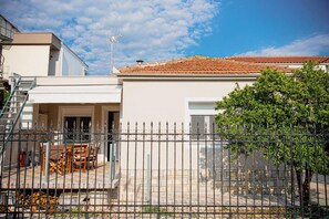 A house with a tiled roof, a fenced patio with outdoor furniture, and a tree in the foreground. - Betty's 4 Seasons in Agria (Agria)