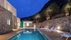 Piscina climatizada con características ecológicas y electrólisis de sal, rodeada de muros de piedra y mobiliario de exterior.