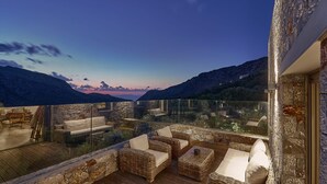 Un balcón con mobiliario de mimbre y baranda de cristal con vistas a un paisaje montañoso.