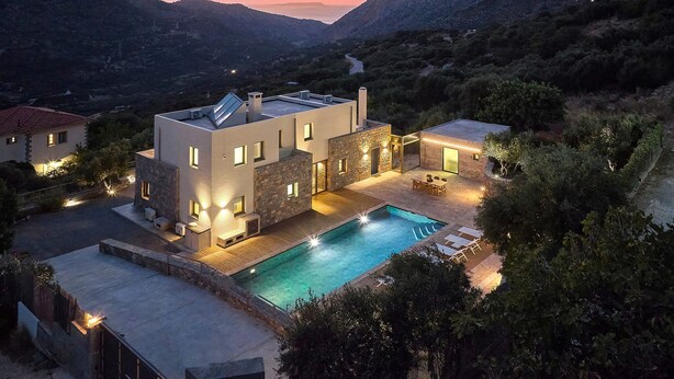 Una villa moderna con piscina, muros de piedra y vistas a las colinas circundantes.