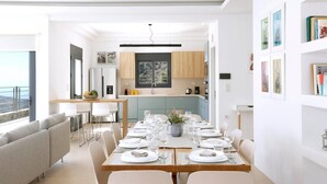 A modern dining area with a long table set for four, a kitchen in the background, and a balcony with a view. - Villa Aires with Private Pool (Vrachasi)