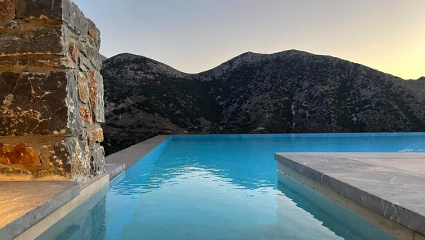 A swimming pool with a stone wall on one side and a view of mountains in the background. - Villa Aires with Private Pool (Vrachasi)