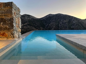 A swimming pool with a stone wall on one side and a view of mountains in the background. - Villa Aires with Private Pool (Vrachasi)