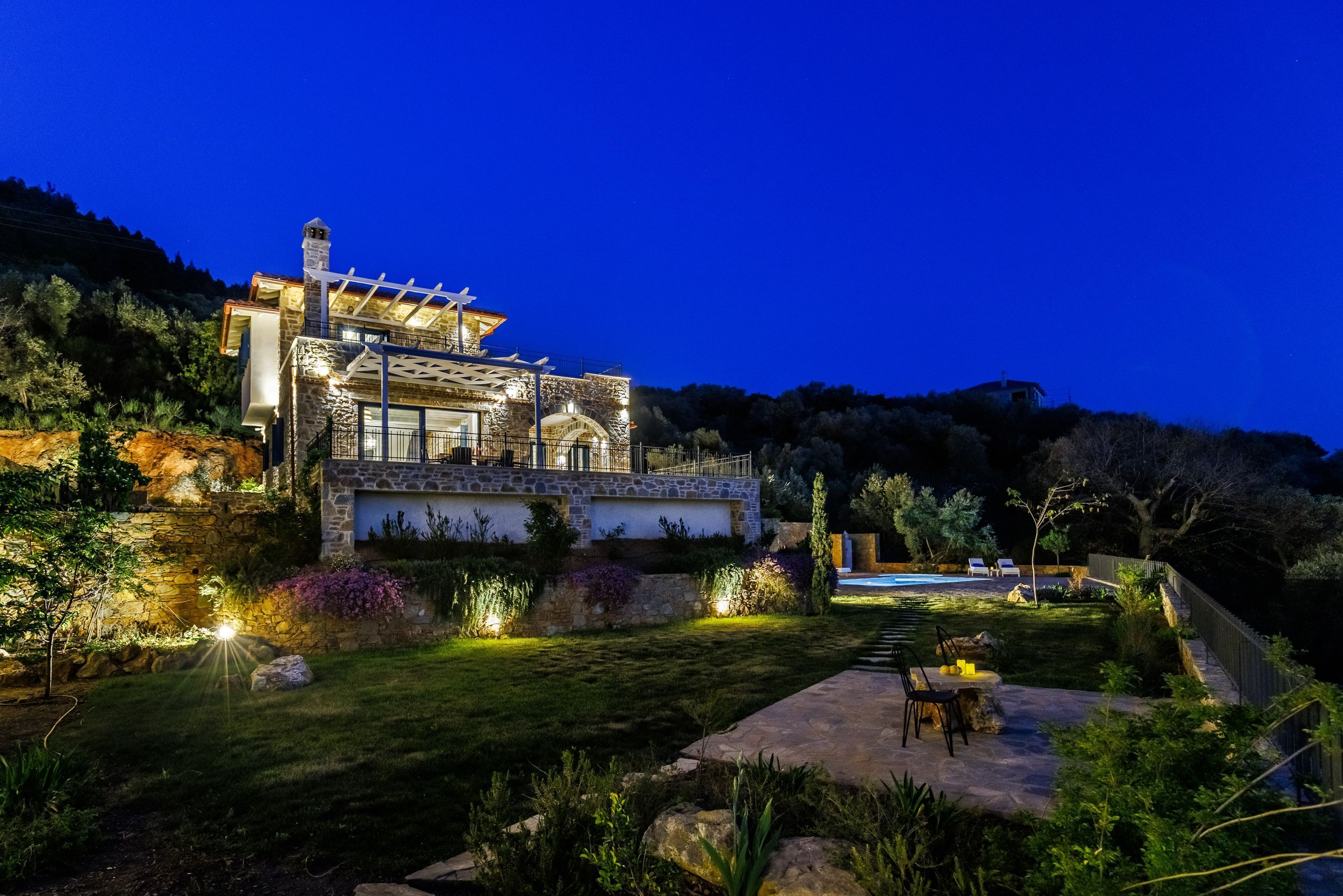 Ein großes, modernes Haus mit Naturstein-Fassade, Schwimmbad und einem gut beleuchteten Garten im Abenddämmerung.