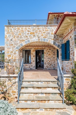 A stone building with a balcony, a staircase leading to the entrance, and a clear sky.