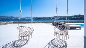En terrass med två gungstolar, en pool och utsikt över havet och kullarna.
