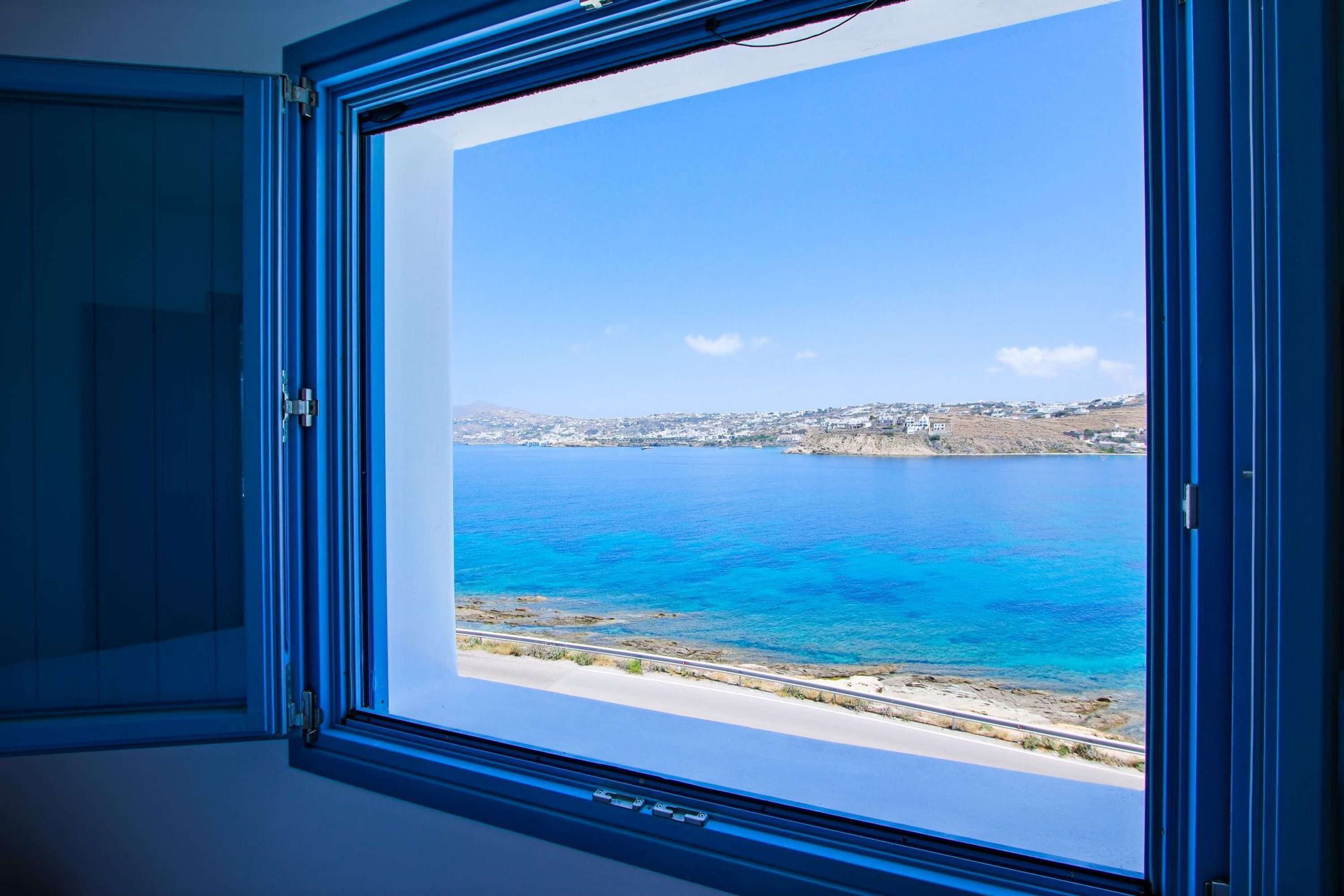 Una habitación con un ventanal que ofrece vistas a un paisaje costero con un mar azul y colinas al fondo.