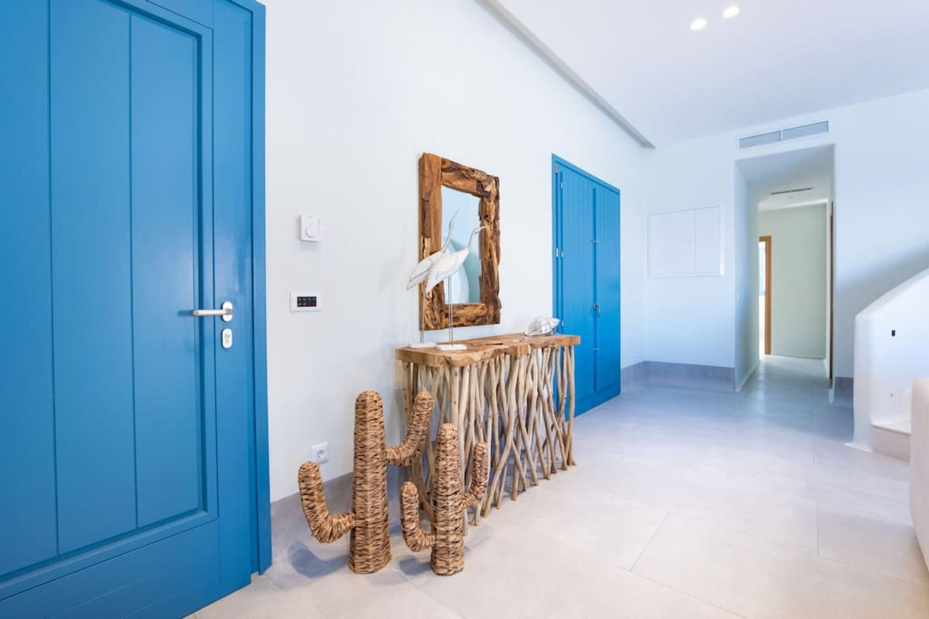Un pasillo con puertas azules, una consola de madera con espejo y esculturas de cactus tejidos.