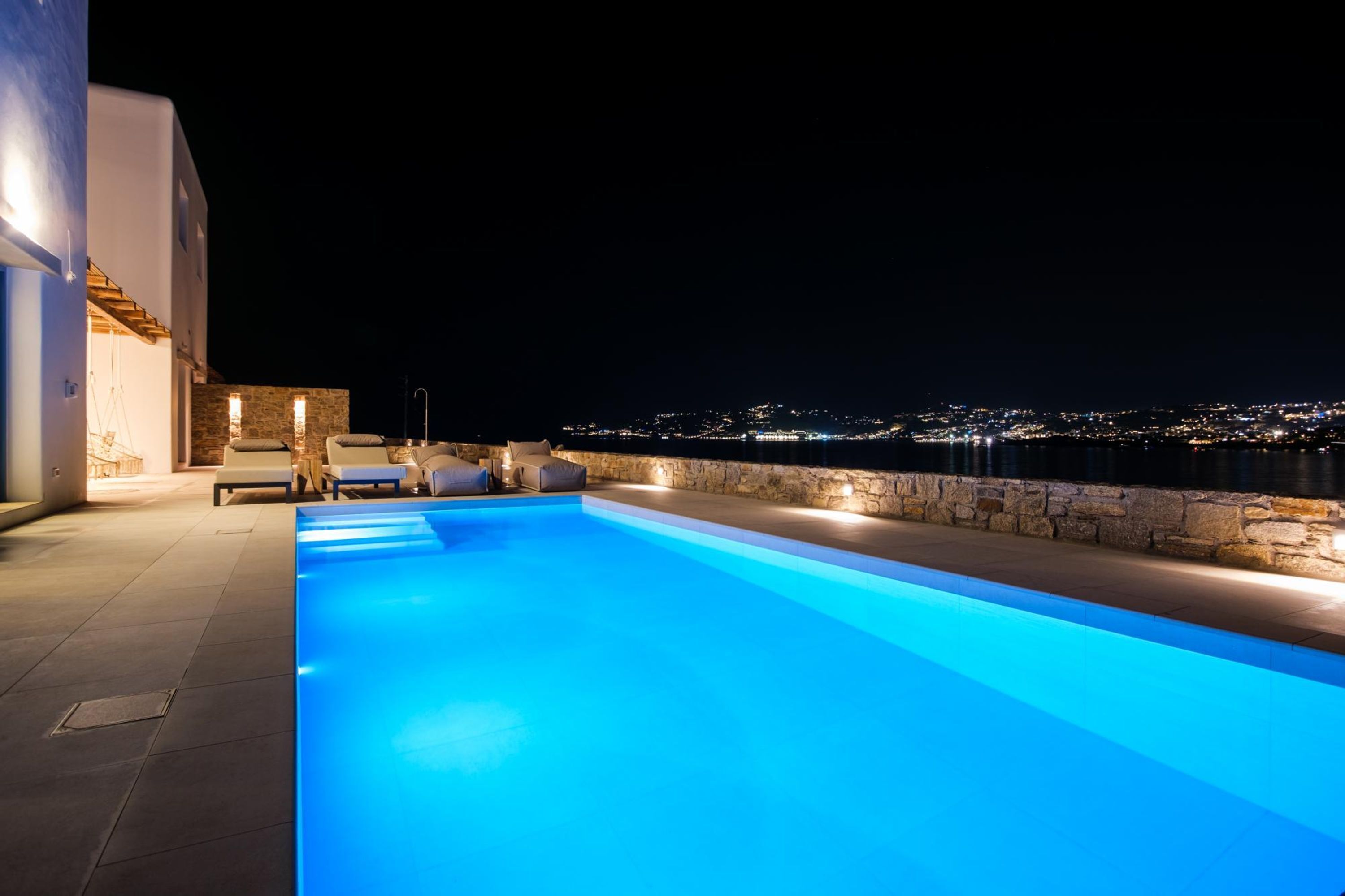 A swimming pool with a stone wall and a view of the city at night.