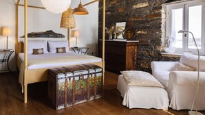 Ein Schlafzimmer mit einem Himmelbett, einer Holzkiste, einer Steinwand und einem Fenster mit Blick.