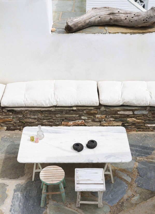 Un espace extérieur aménagé avec des sièges blancs, un mur en pierre en arrière-plan, une petite table sur laquelle reposent deux objets noirs, un tabouret vert et une chaise blanche.