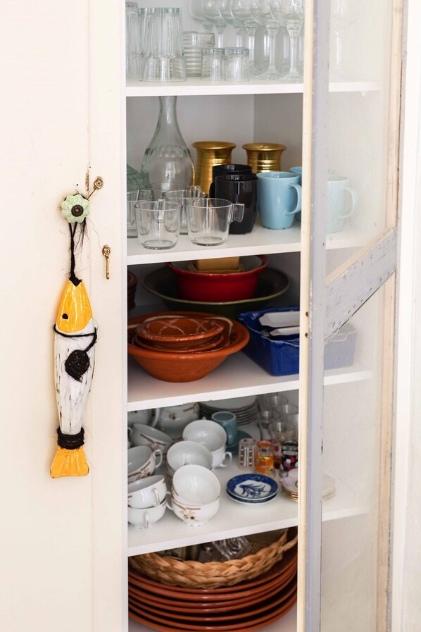 A kitchen cabinet with shelves holding various kitchenware, including glassware, plates, and bowls. - Tinos experience: the house (Panormos)