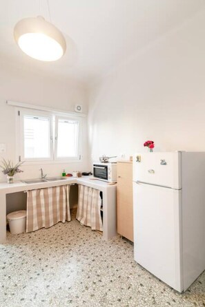 A compact kitchen with a refrigerator, microwave, and a window above the sink. - Mimosa: The mosaic home (Tinos)