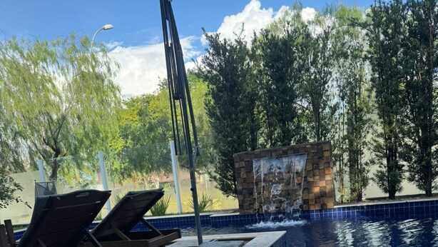 En pool med solstolar och en dekorativ vattenfallsanordning.