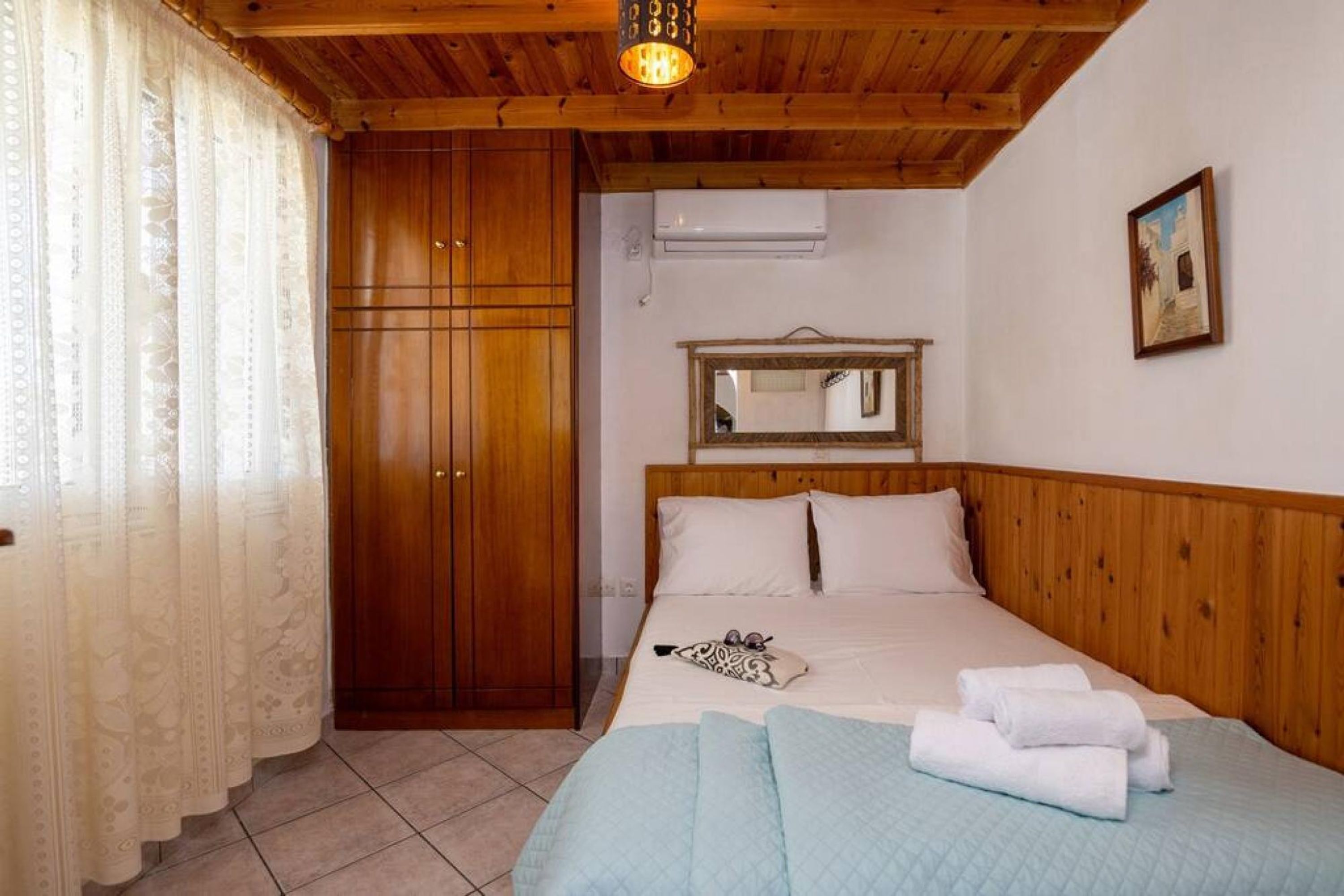 Ein Schlafzimmer mit Holzbalkendecke, einem Bett mit weißer Bettwäsche, einem Holzschrank und einem Spiegel an der Wand.