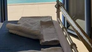 Une chambre avec un lit placé face à une grande fenêtre donnant sur une plage et l’océan.