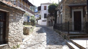 A narrow cobblestone street flanked by stone buildings with balconies and windows. - Nikolaou Apartments Upper Floor (Keramidi)