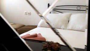 A bed with white bedding, a brown bedside table, and a small vase with dried flowers. - Nikolaou Apartments Upper Floor (Keramidi)