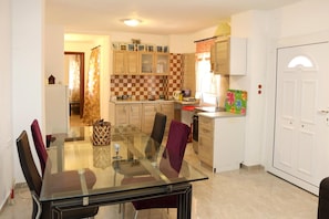 A dining area with a glass table and chairs, a kitchen with checkered tiles, and a white door.