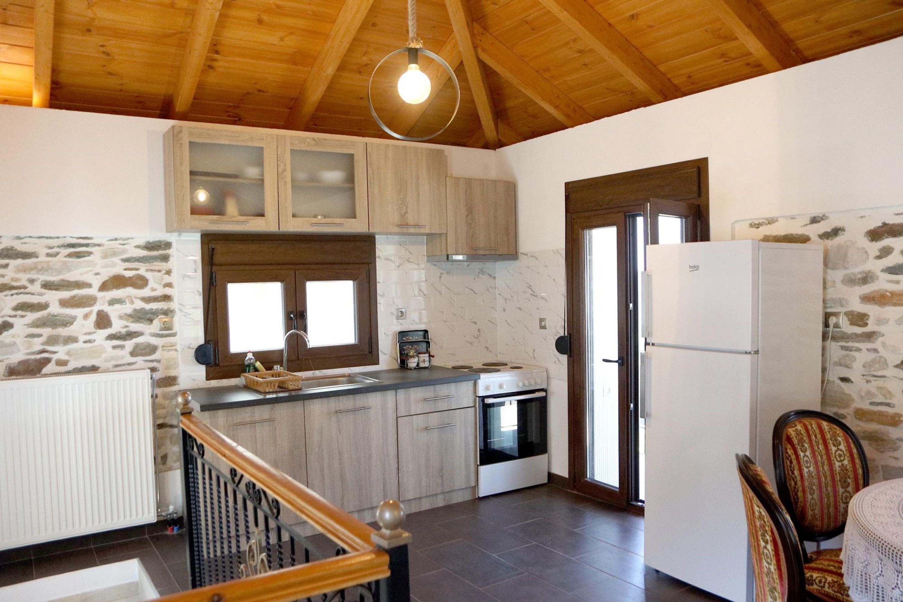 Una cucina con mobili in legno, una parete in pietra, un forno a incasso e un frigorifero.