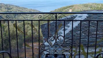 Un balcone con tavolo e sedie, affaccia su un paesaggio costiero con colline e mare.