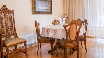 A dining area with a round table, floral tablecloth, and ornate wooden chairs.