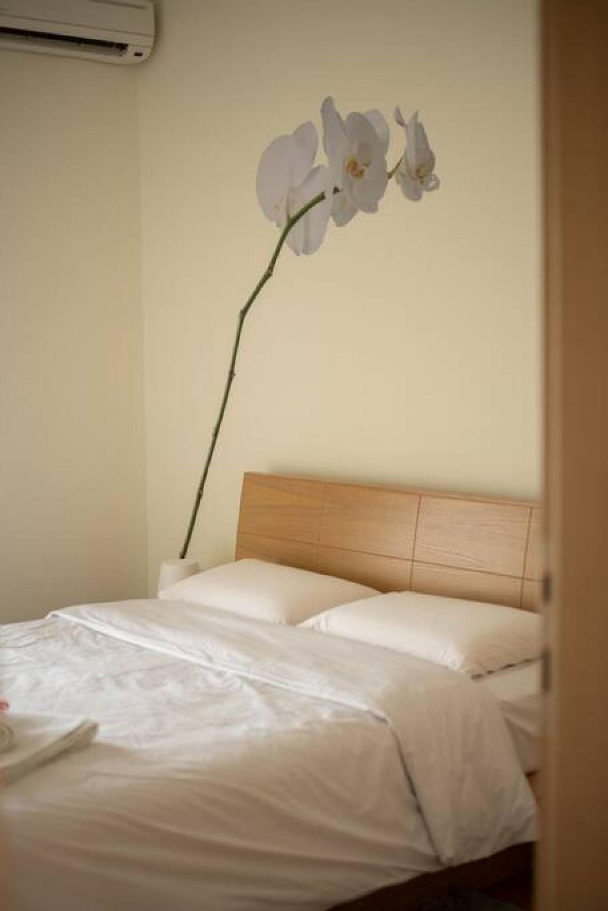 Un lit avec une literie blanche et une seule branche d’orchidée accrochée au mur.
