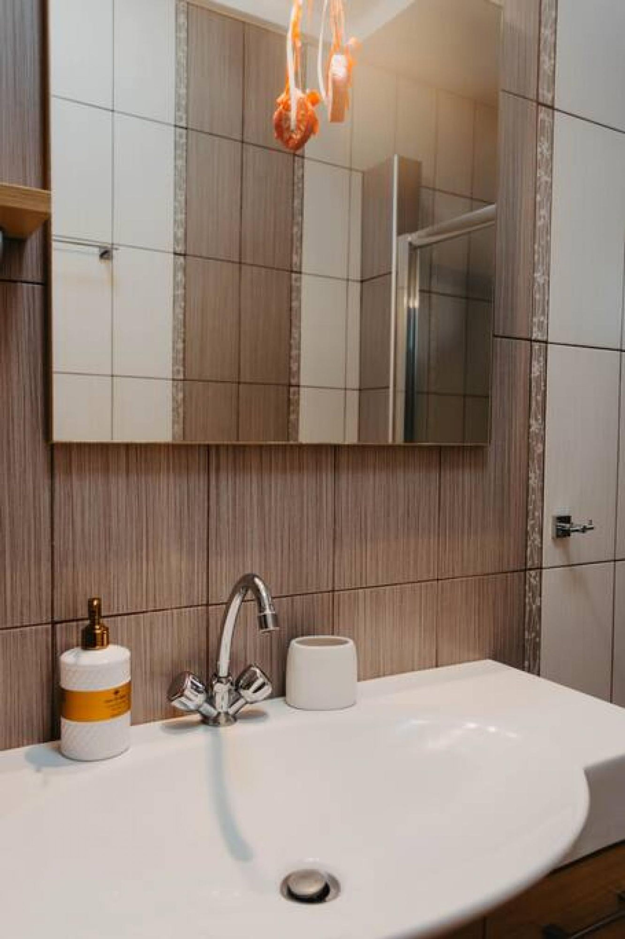 Une salle de bain moderne avec un lavabo blanc, un robinet chromé, un distributeur de savon blanc et un miroir au-dessus du lavabo.