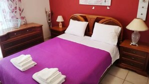 A hotel room with a bed, two nightstands, a wooden headboard, a red wall, and a floral artwork. - Alex’ s apartment in Trikala (Trikala)