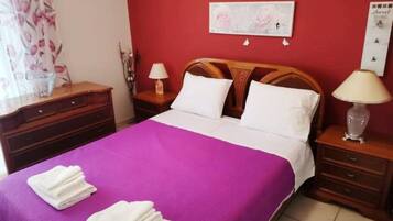 Habitación de hotel con cama, dos mesitas de noche, cabecera de madera, pared roja y una obra de arte floral.