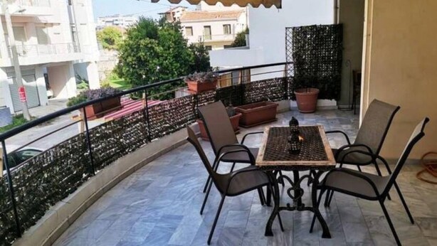A balcony with a table and chairs, potted plants, and a view of buildings. - Alex’ s apartment in Trikala (Trikala)